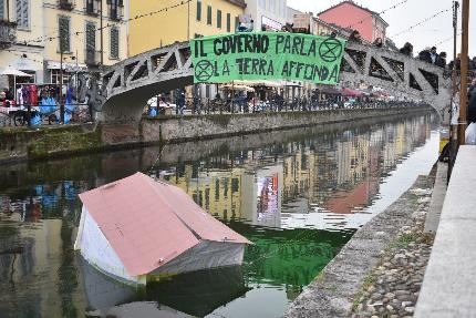 Extinction Rebellion - Extinction Rebellion il 09/12/2023: A Milano il Naviglio Grande si è tinto di verde mentre una casa di cartapesta 'affondava' tra le acque e dal ponte Alda Merini e uno striscione urlava 'il governo parla, la Terra affonda'.