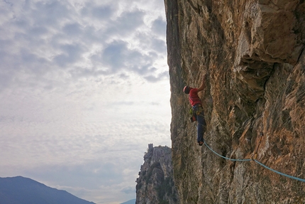 Via Mescalito Arco, Monte Colodri - Mescalito sulla Rupe Secca, Monte Colodri: Carlo Cosi in azione sul traverso del quarto tiro, il castello di Arco sullo sfondo