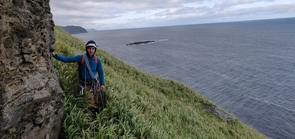 Lofoten, Moskensøya, Storskiva, Ørneeggen, Juho Knuuttila, Misha Mishin - Misha Mishin sui pendii erbosi prima di salire la parete ovest dello Storskiva sull'isola di Moskensøya nelle Lofoten (Norvegia).